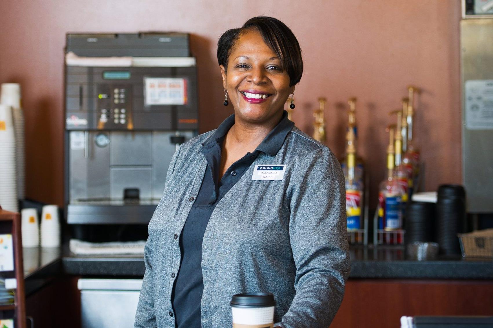 Woman behind coffee shop counter holding a coffee cup.